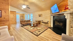 A cozy living room with a fireplace, wooden walls, and a ceiling fan. - Beautiful mountain cabin (Sevierville)