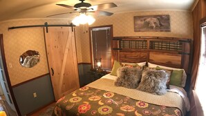 Ein Schlafzimmer mit einem Holz-Kopfteil, einer blumigen Bettdecke und einem Deckenventilator.