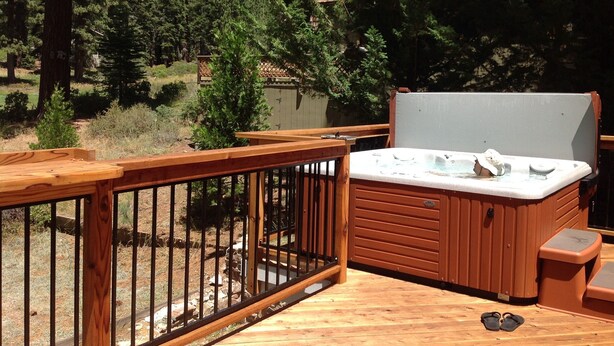 Eine Holterrasse mit Whirlpool, umgeben von Bäumen und einem Zaun.