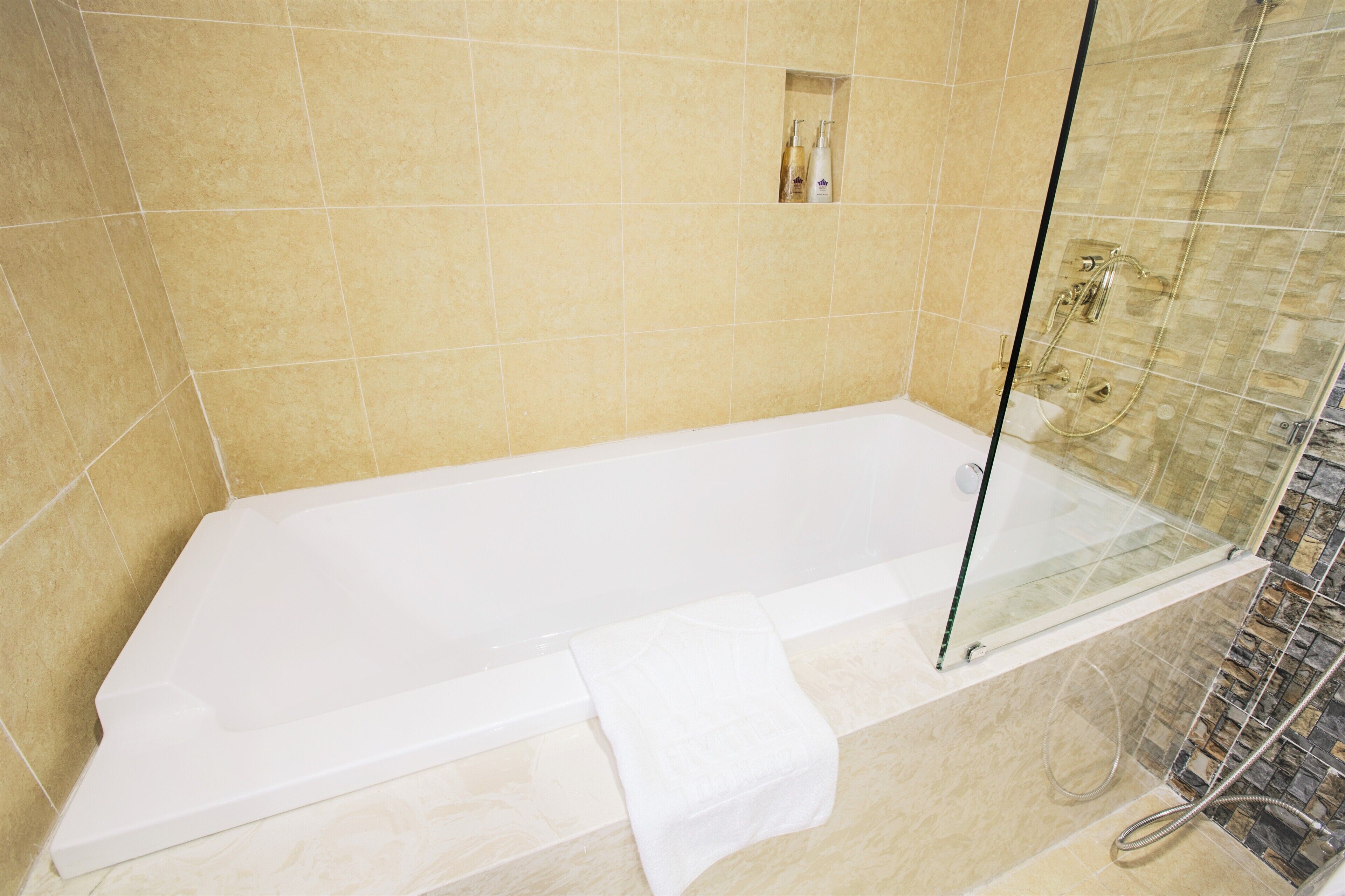 A modern bathroom with a glass-enclosed shower, a white bathtub, and beige tiles.