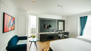 A hotel room with a bed, a desk with a chair, a TV, and a large window with curtains.