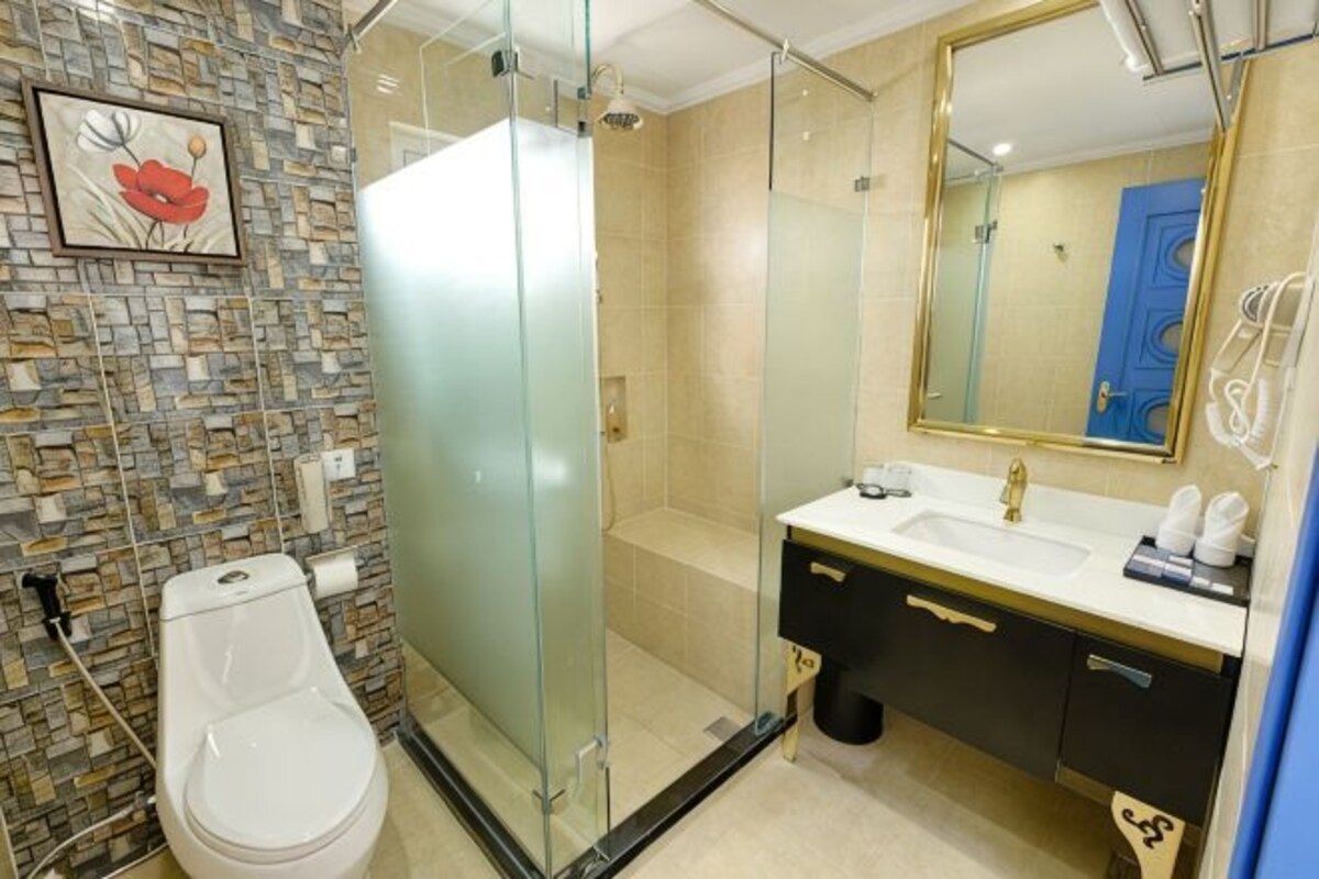 A bathroom with a glass-enclosed shower, a toilet, a sink with a gold mirror, and a tiled wall.