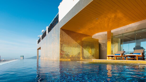 A modern infinity pool with a clear view of the ocean, a covered seating area with lounge chairs, and a distinctive tiled wall design. - Fivitel Da Nang (Da Nang)