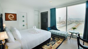 A hotel room with a large bed, a seating area with a view of a cityscape and a bridge, and a small table with a plant. - Fivitel Da Nang (Da Nang)
