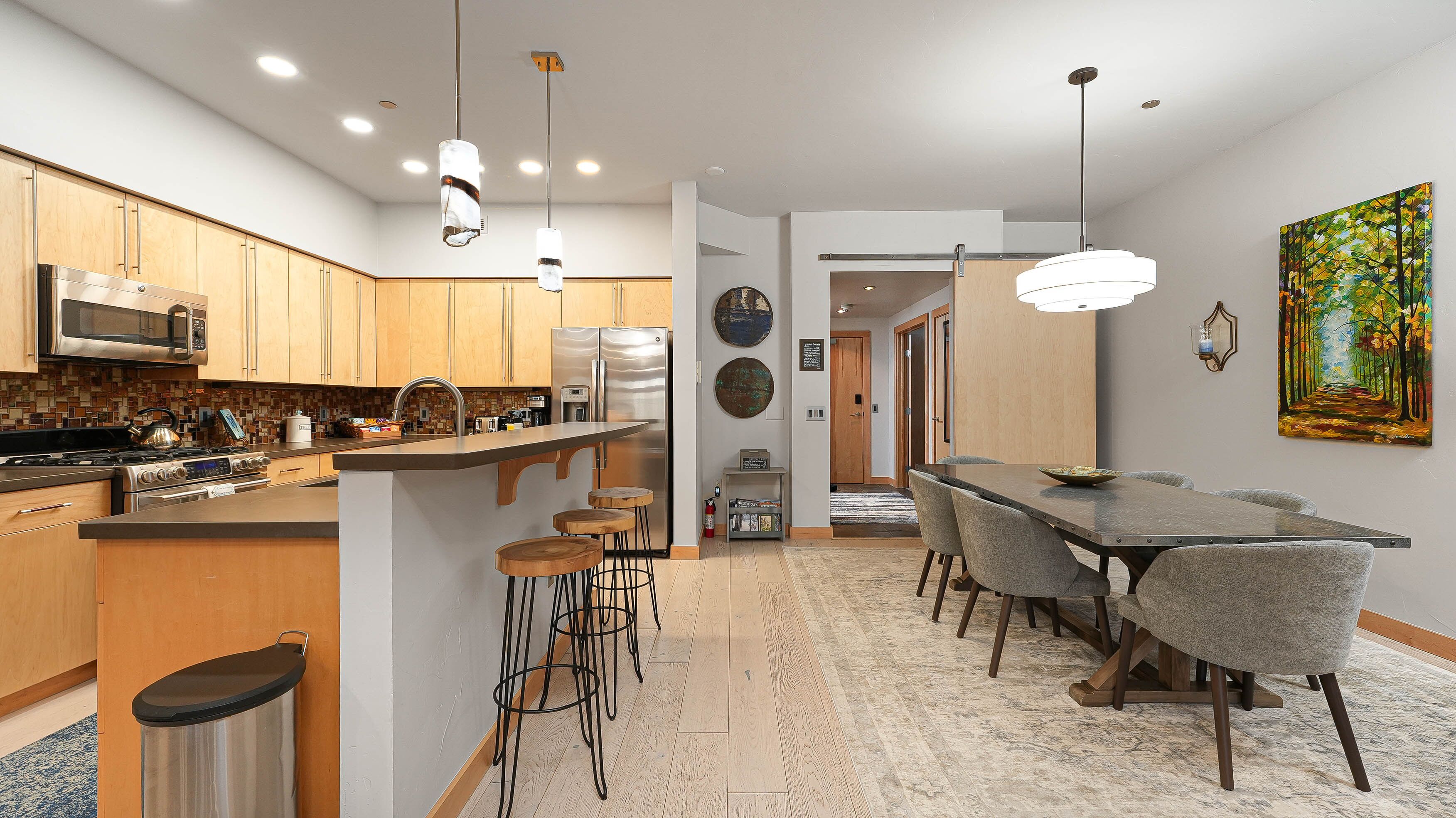 A modern kitchen with stainless steel appliances, a central island with stools, and a dining area with a long table and chairs.