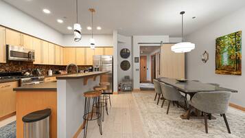 A modern kitchen with stainless steel appliances, a central island with stools, and a dining area with a long table and chairs.