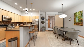 A modern kitchen with stainless steel appliances, a central island with stools, and a dining area with a long table and chairs. - LUXURY IN DOWNTOWN, A/C, GARAGE, SKI LOCKER ON MTN, FREE BUS,  2 KING 1 QN BED (Steamboat Springs)