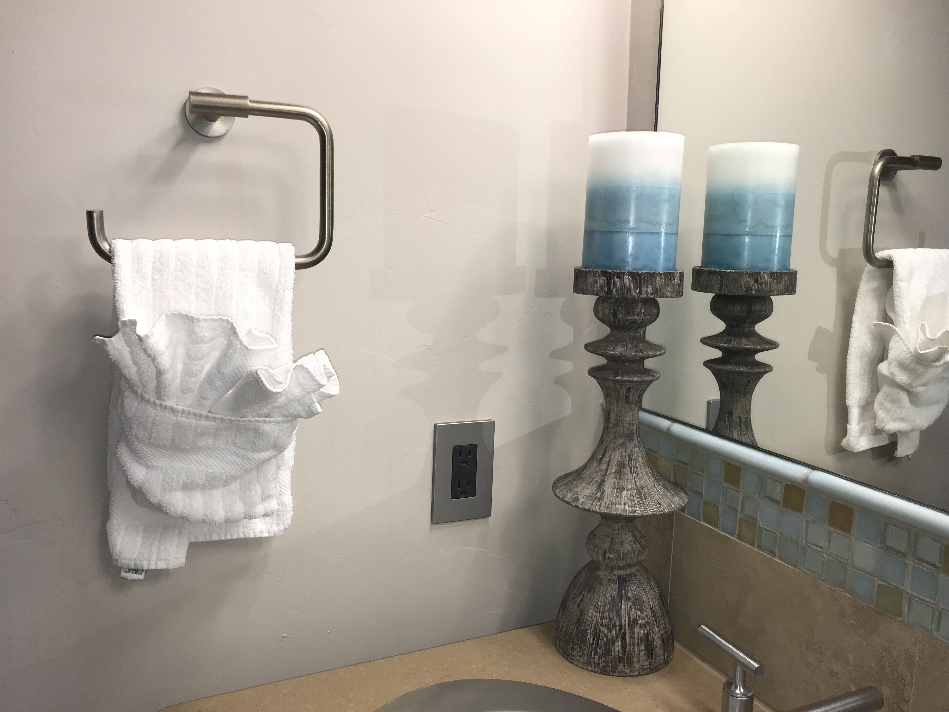 A bathroom with a towel rack, a sink, a mirror, and two candles on a decorative stand.