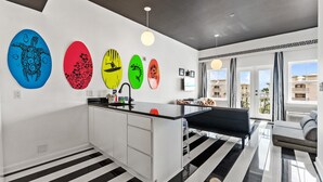 A modern kitchen with a central island, a dining area with a bench, and a view of the city through large windows. - Gulf Place Studio-30a! Beach View, Pool-Hot Tub, Balcony, Tennis, Pickle Ball (Santa Rosa Beach)
