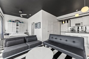 A modern hotel room with a black and white color scheme, featuring a sofa, a bed, a dining area, and a kitchen.