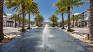 A fountain in the center of a street lined with palm trees and buildings. - Gulf Place Studio-30a! Beach View, Pool-Hot Tub, Balcony, Tennis, Pickle Ball (Santa Rosa Beach)