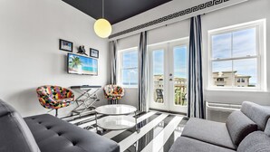 A modern living room with a black and white striped floor, two colorful armchairs, a black sofa, and a round glass table. - Gulf Place Studio-30a! Beach View, Pool-Hot Tub, Balcony, Tennis, Pickle Ball (Santa Rosa Beach)