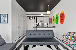 A modern kitchen with white cabinets, a black countertop, and a black ceiling. There are colorful surfboards on the wall and a black sofa in the foreground.
