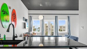 A modern kitchen with a black countertop, a sink, and two surfboards on the wall. - Gulf Place Studio-30a! Beach View, Pool-Hot Tub, Balcony, Tennis, Pickle Ball (Santa Rosa Beach)