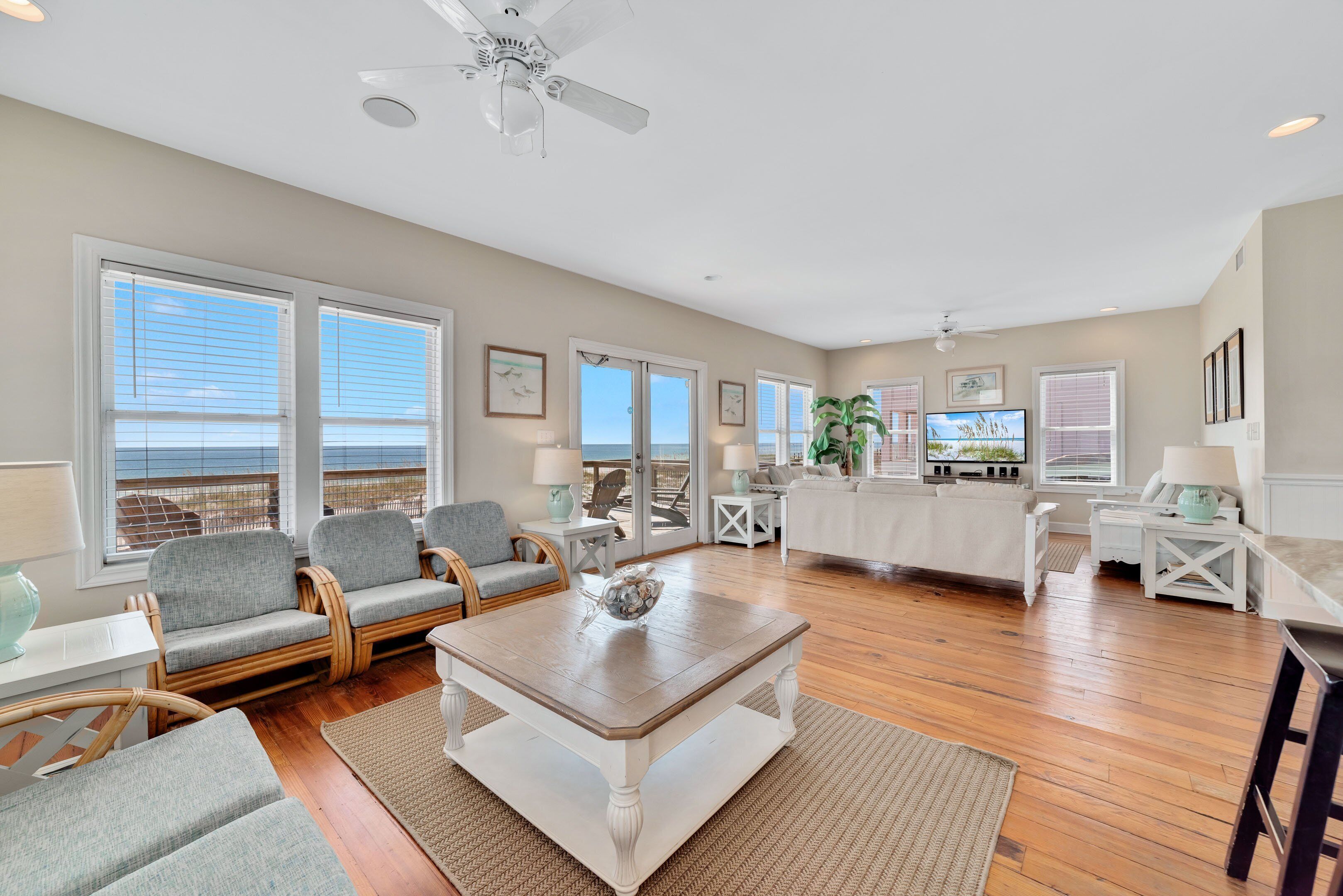 A spacious living room with a large window, a ceiling fan, and a view of the ocean.