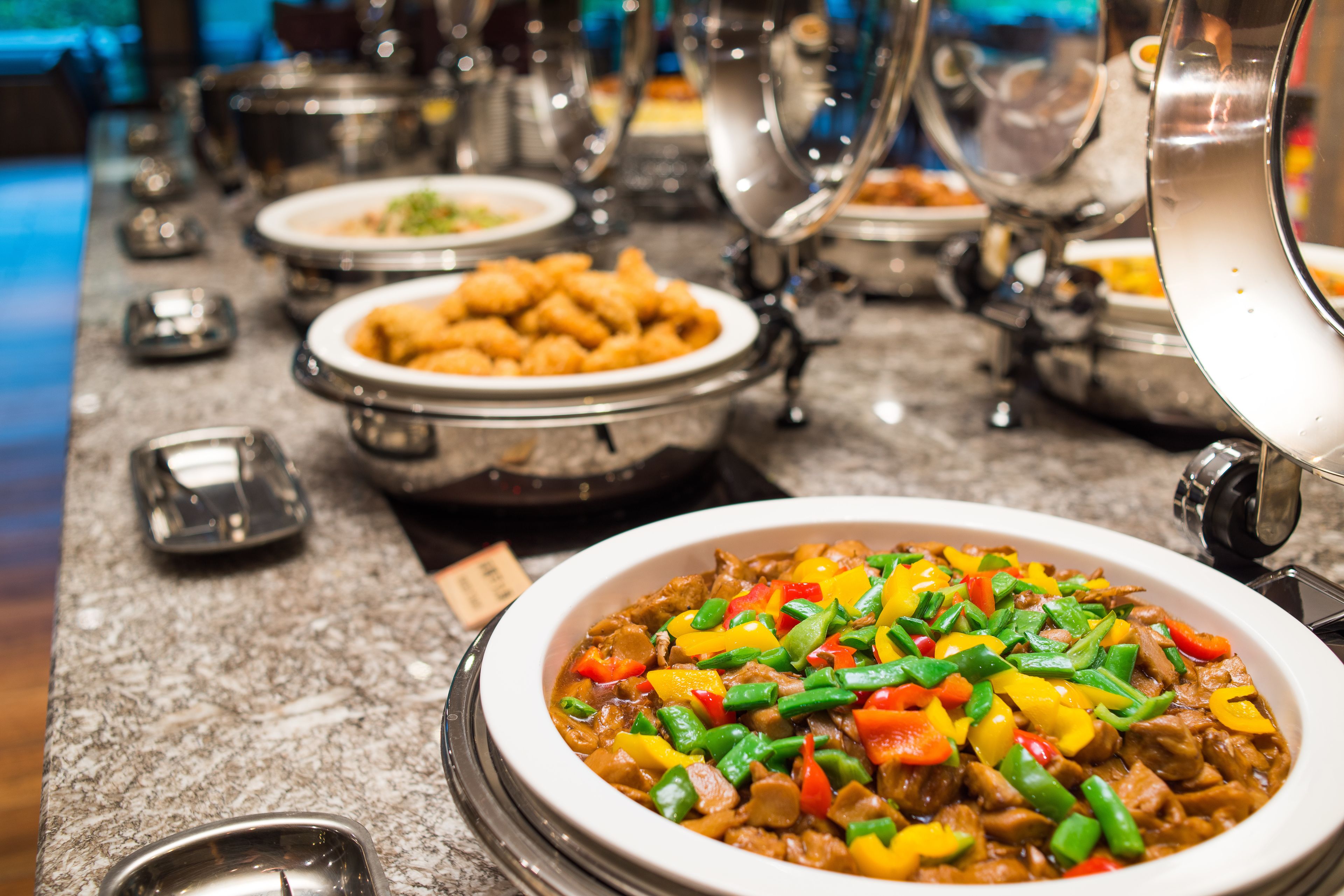 Uma mesa de buffet com diversos pratos, incluindo uma grande tigela de legumes e carne refogados.
