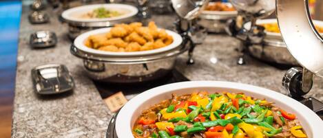 Uma mesa de buffet com diversos pratos, incluindo uma grande tigela de legumes e carne refogados.