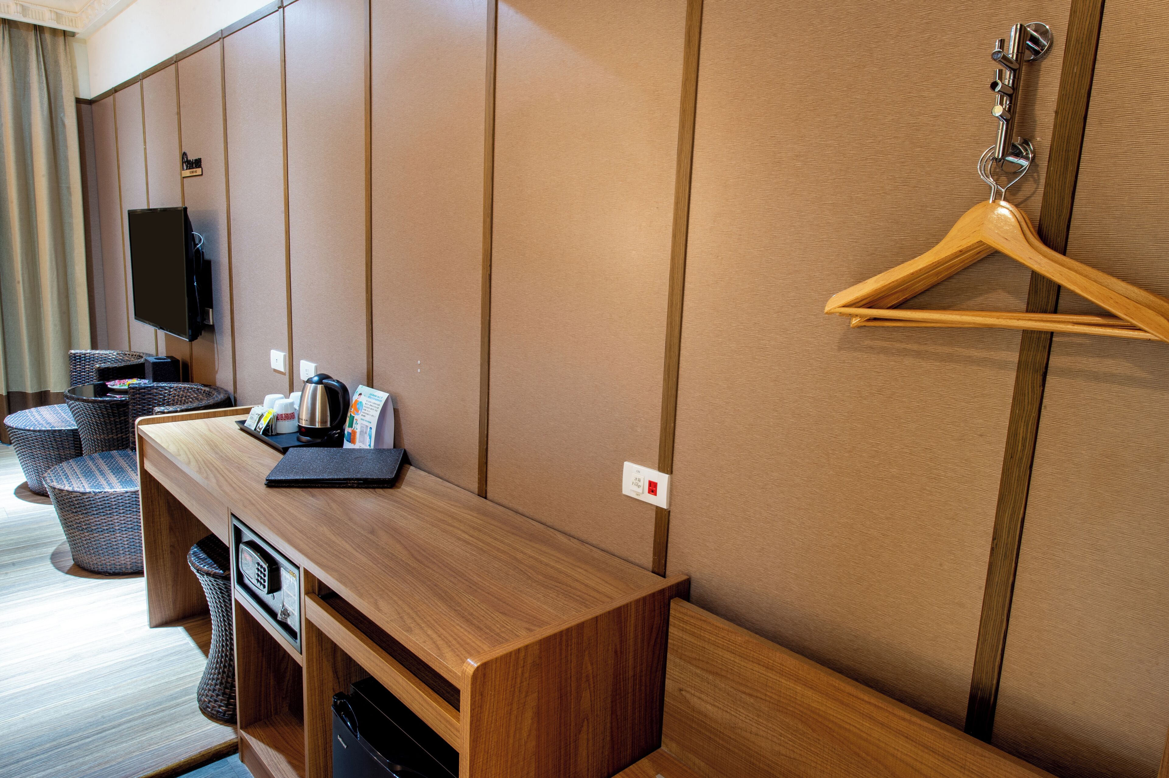 Une chambre d’hôtel avec un bureau en bois, un téléviseur et un porte-manteau en bois fixé au mur.