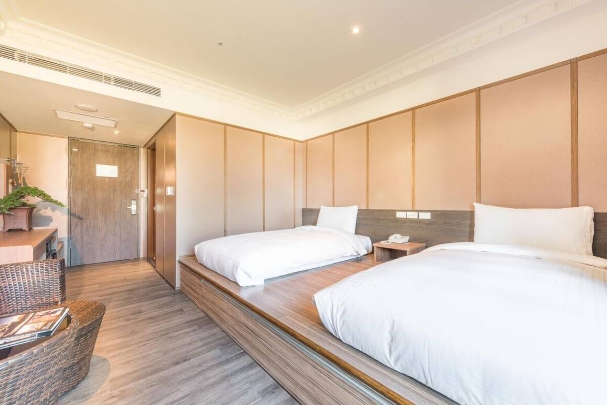 Una habitación de hotel moderna con dos camas, un cabecero de madera, un escritorio pequeño y una silla de mimbre.