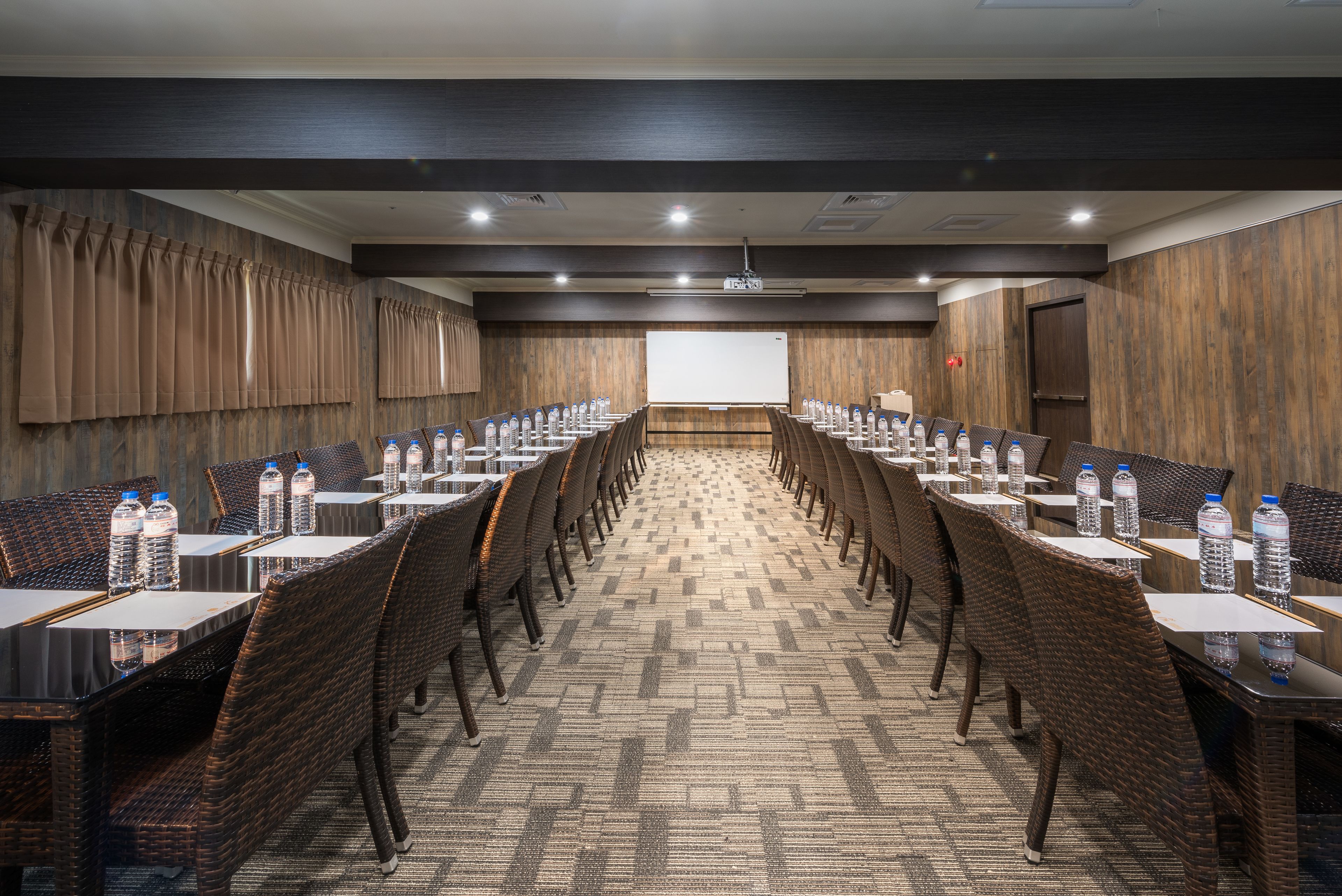 Un salón de conferencias con mesas largas, sillas y botellas de agua.