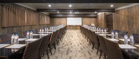 Un salón de conferencias con mesas largas, sillas y botellas de agua.