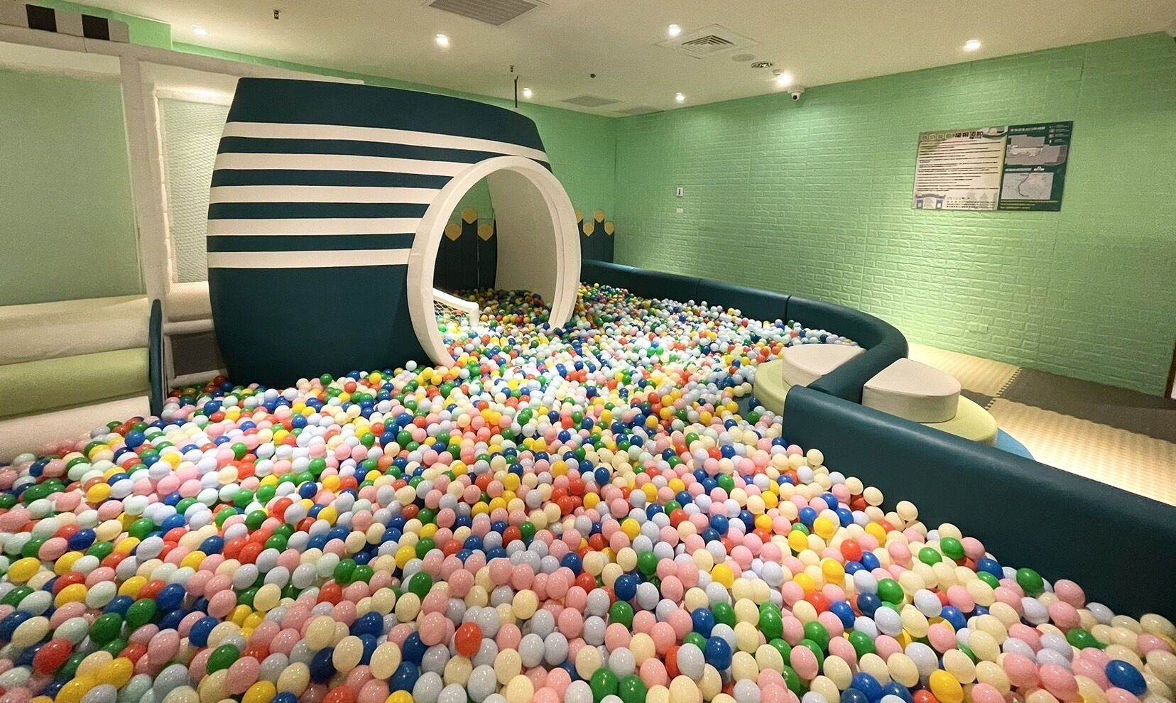 Un espace de jeux avec des balles, un toboggan, des murs verts et un coin salon.