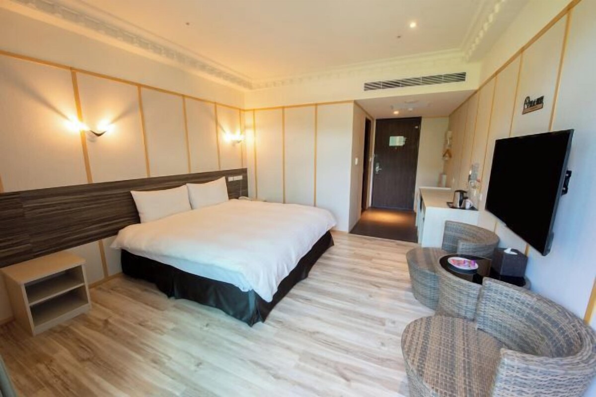 A hotel room with a large bed, a flat-screen TV, a seating area with a sofa and armchairs, and a small table.
