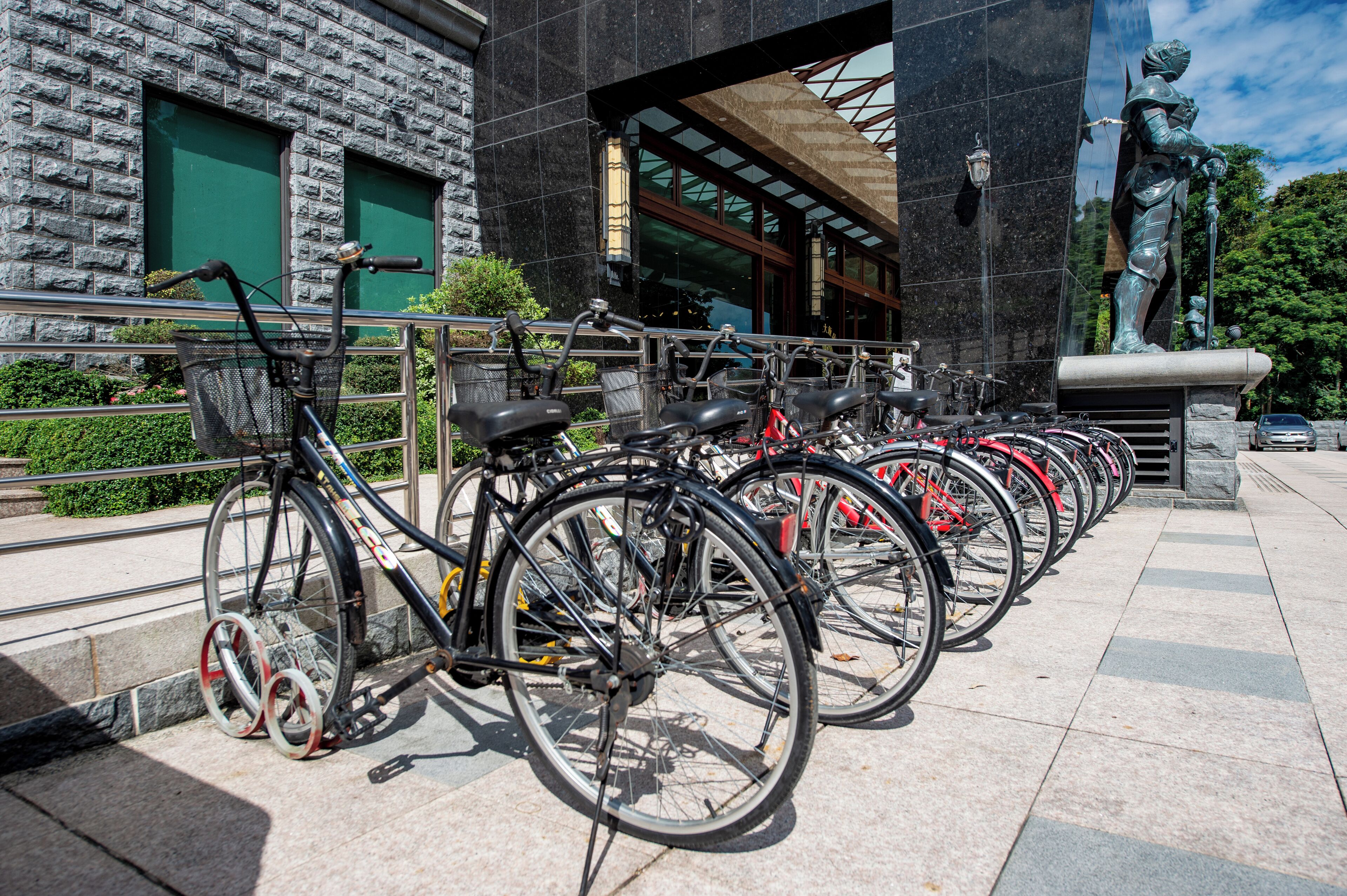 A row of bicycles parked in front of a building with a stone facade and a statue.