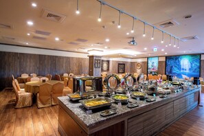 A buffet setup with multiple serving stations, a variety of dishes, and a seating area with round tables and chairs.