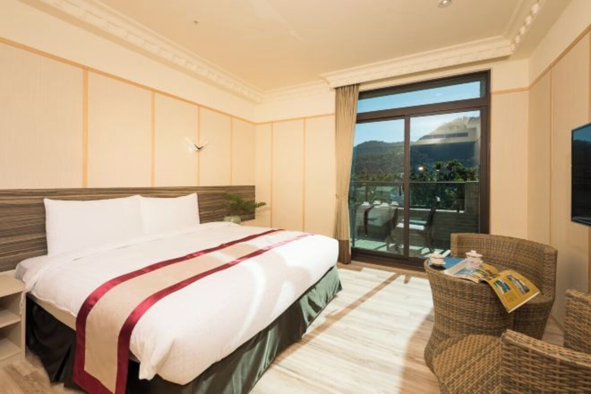 A hotel room with a large bed, a balcony with a view, and a television.