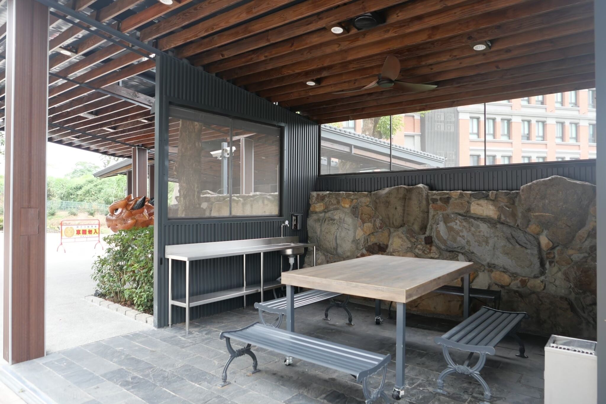 An outdoor patio with a stone wall, a wooden ceiling, and metal furniture.