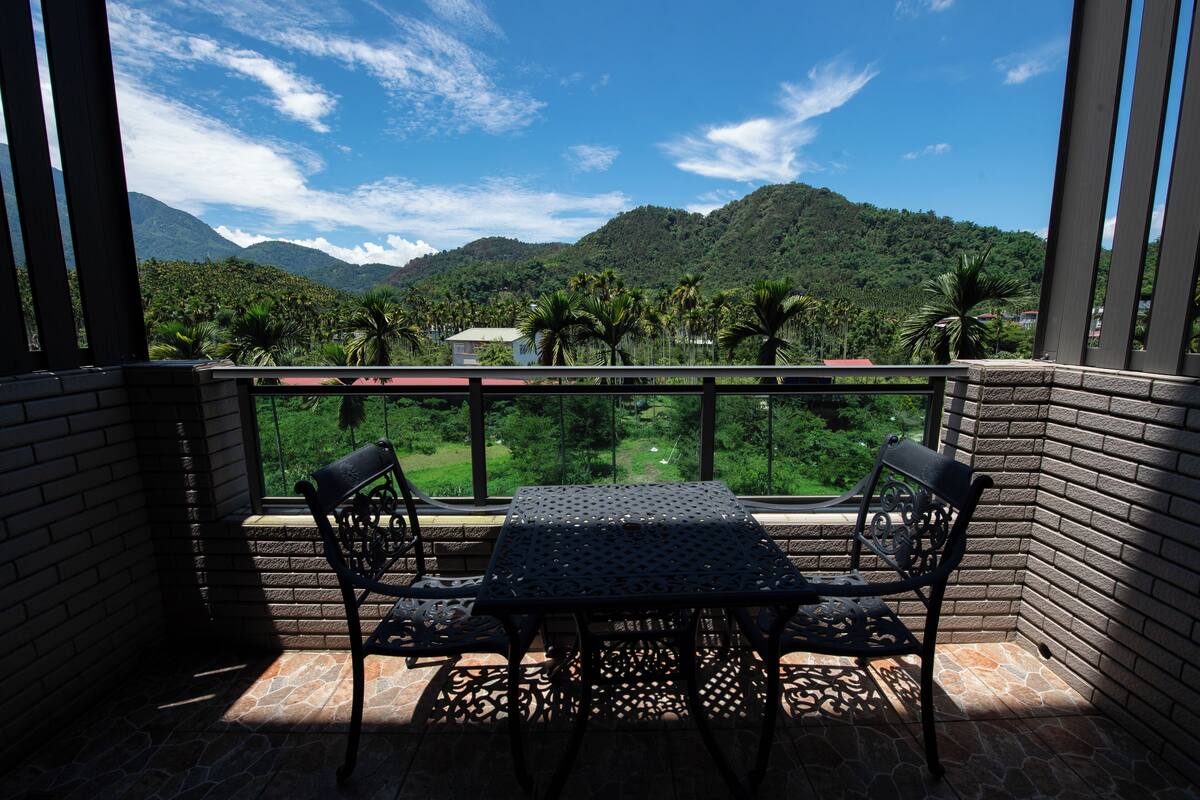 Un balcón con mesa y sillas, con vistas a un paisaje verde exuberante y montañas.
