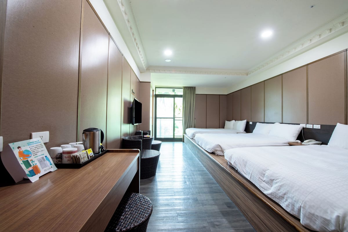 Habitación de hotel con dos camas, un escritorio con cafetera, televisor y vistas al exterior.