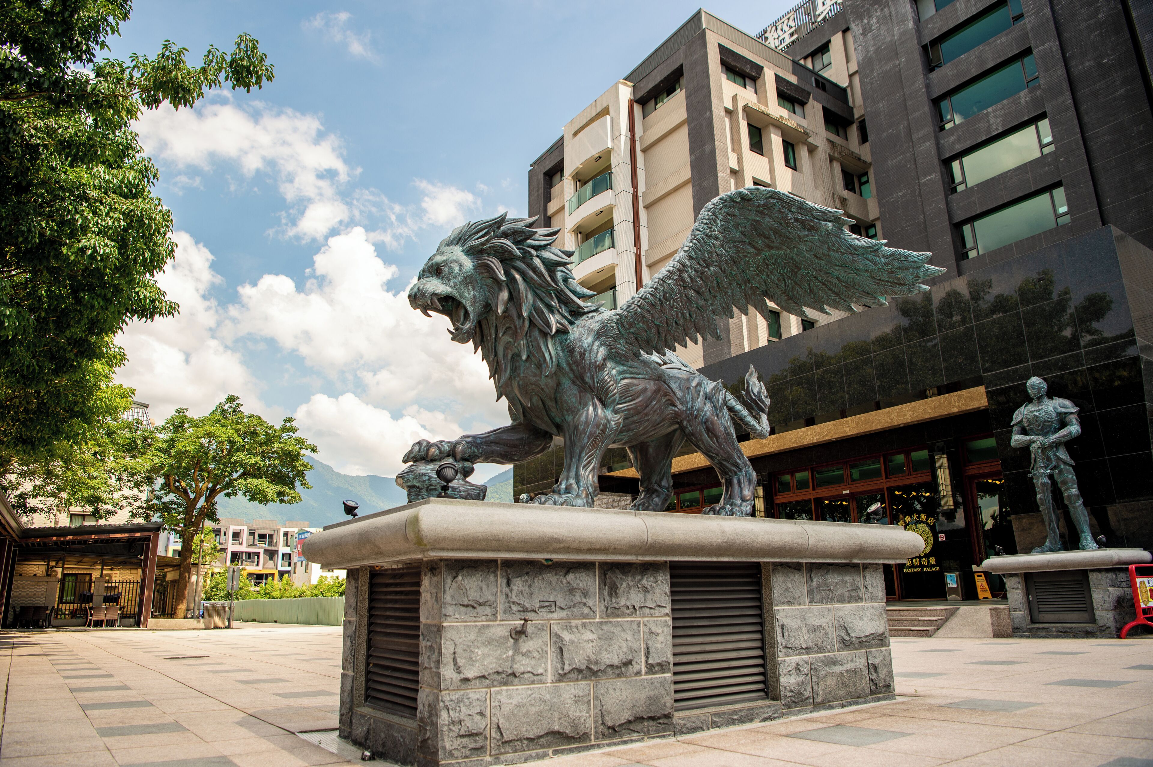 A bronze statue of a winged lion on a pedestal in an urban plaza.