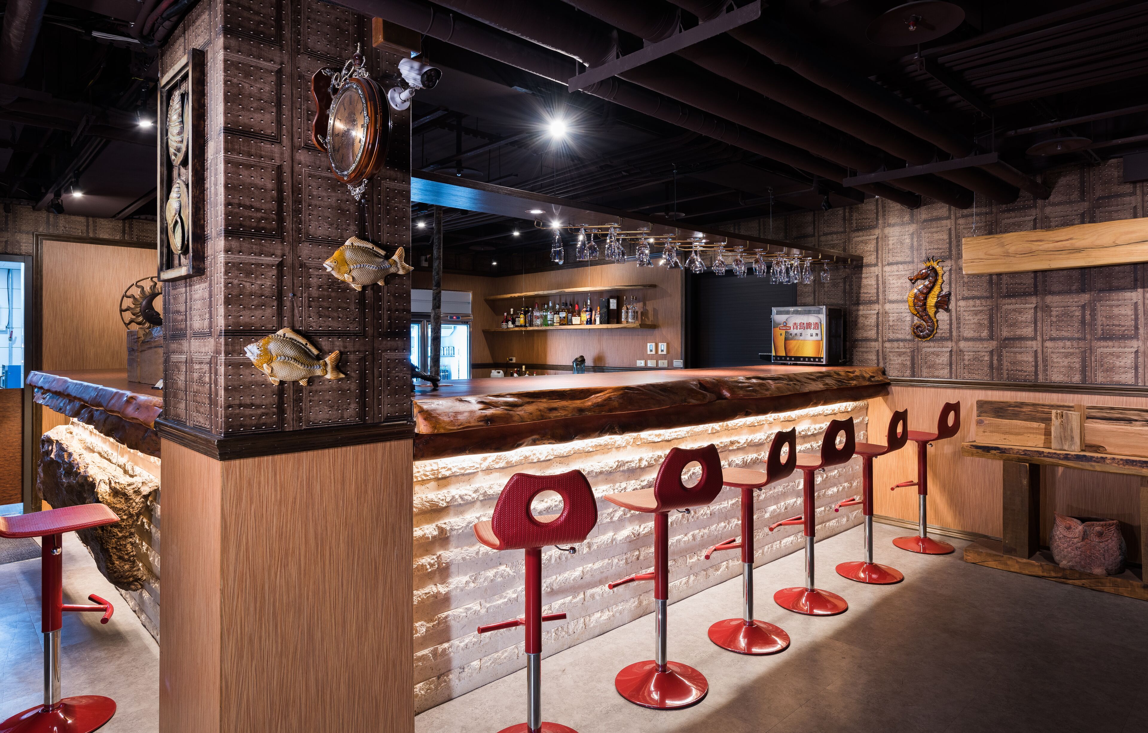 A bar area with a wooden counter, red bar stools, and decorative fish on the wall.