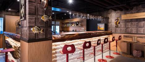 A bar area with a wooden counter, red bar stools, and decorative fish on the wall.