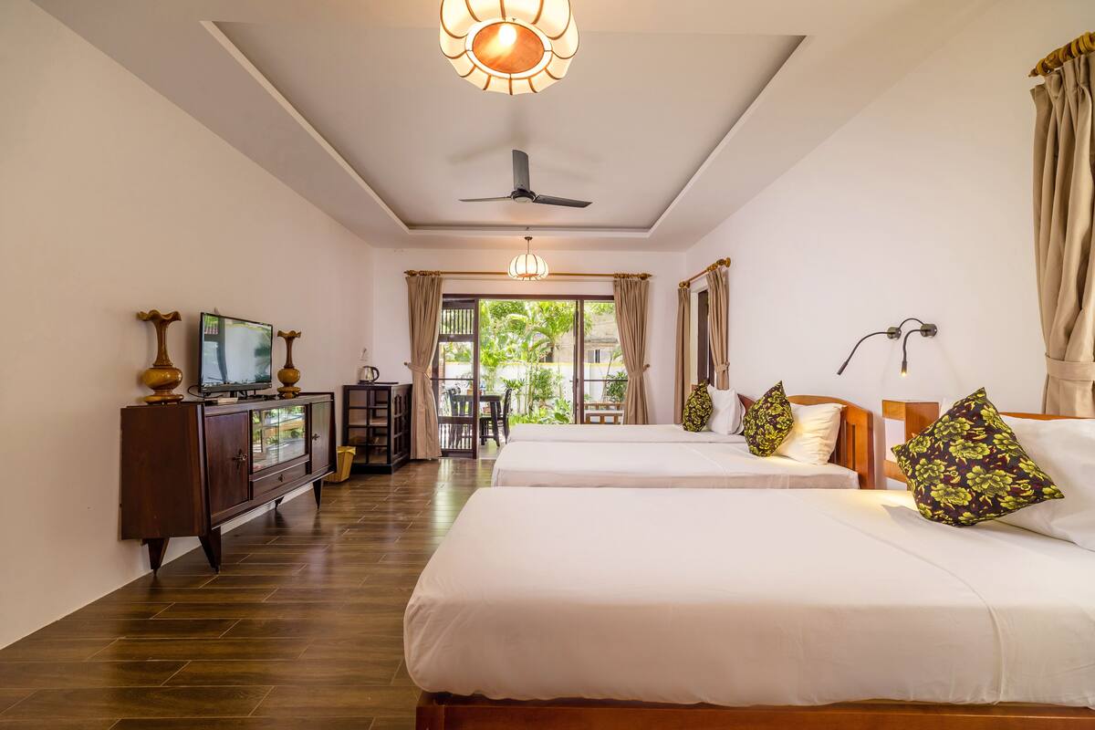 A hotel room with two beds, a TV, a desk, and a view of the outdoors.