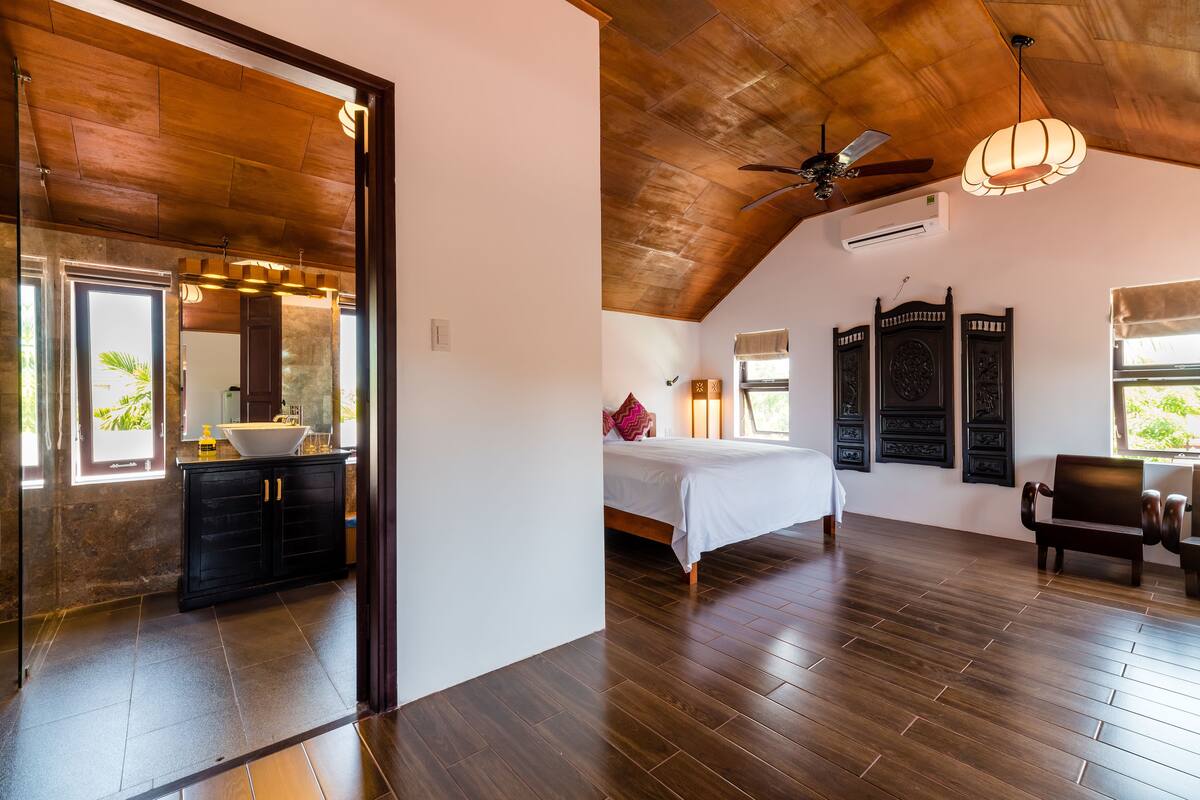 A bedroom with a wooden ceiling, a bed, a nightstand, and a window with curtains.