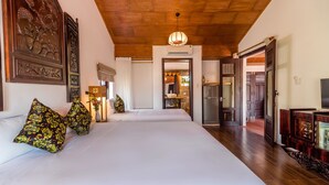 Quarto de hotel com uma cama grande, teto de madeira e um corredor que dá para uma área de cozinha.