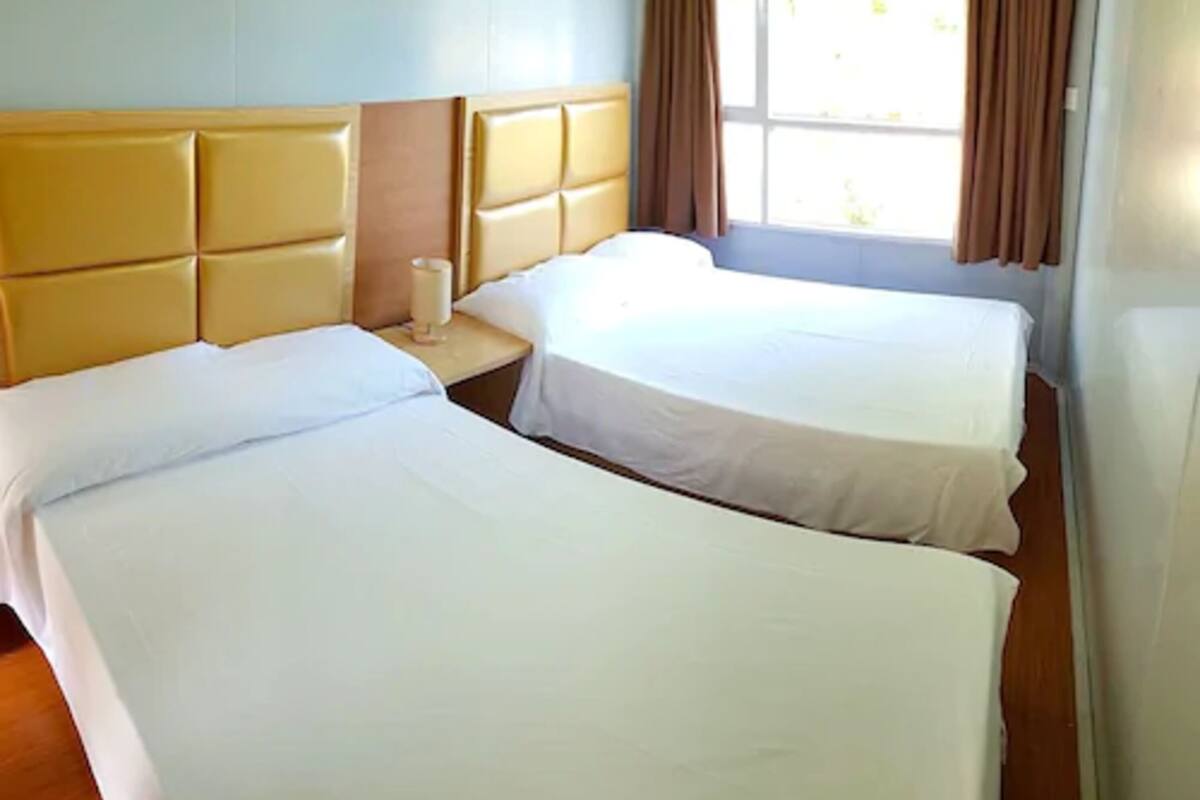 Une chambre d’hôtel avec deux lits, une tête de lit en bois, une table de chevet et une fenêtre avec des rideaux.