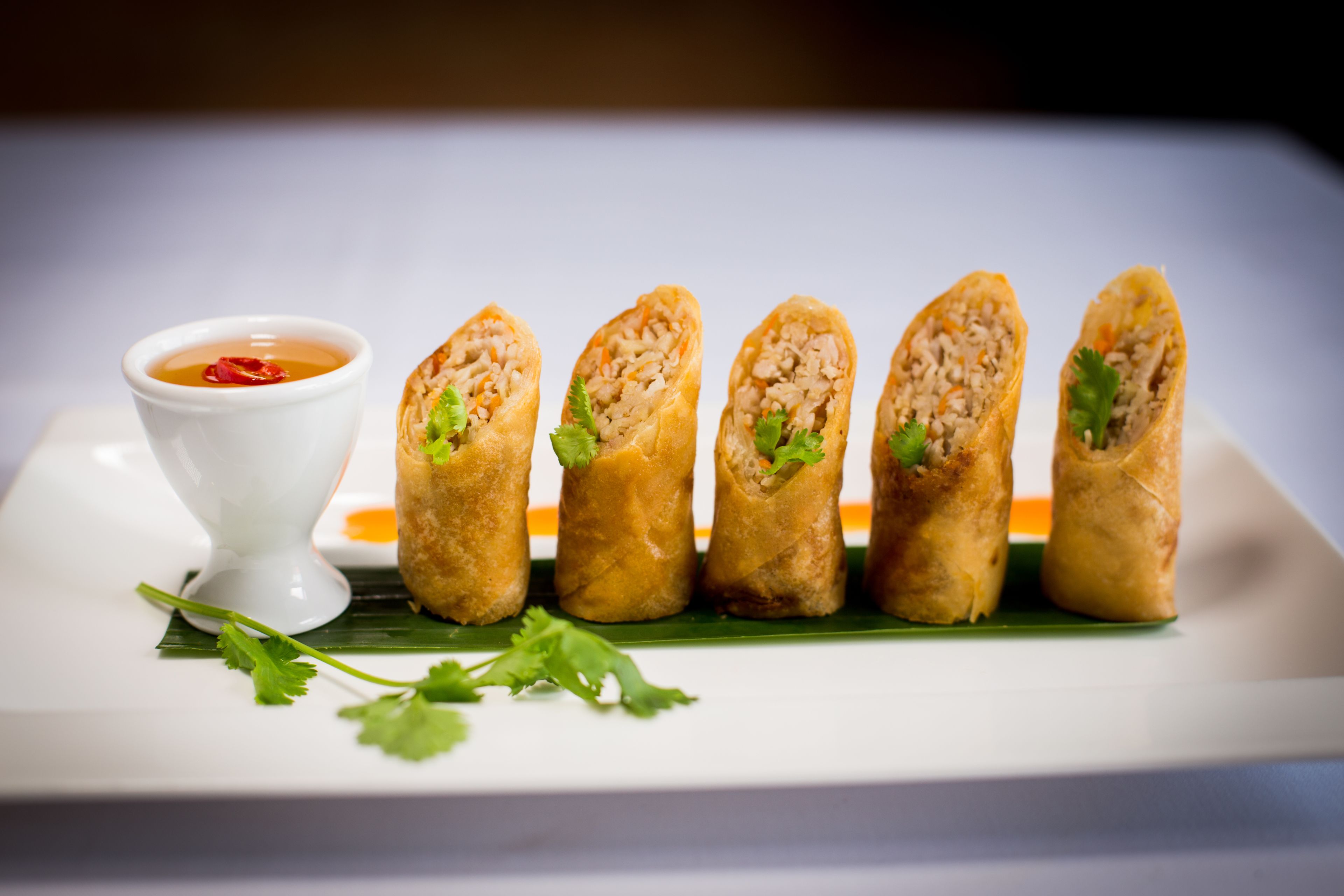 A plate of spring rolls with a dipping sauce and fresh herbs.