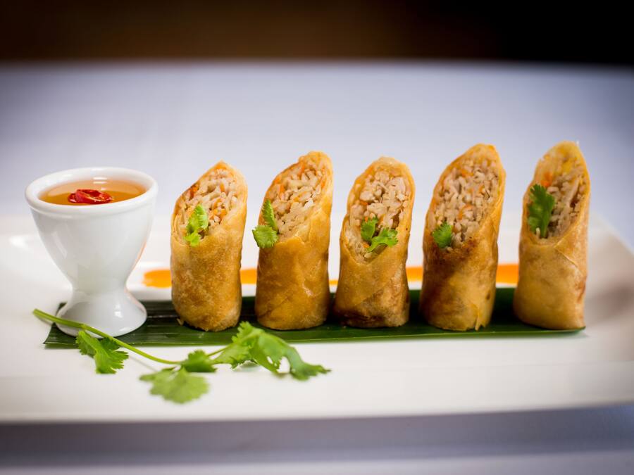 A plate of spring rolls with a dipping sauce and fresh herbs.