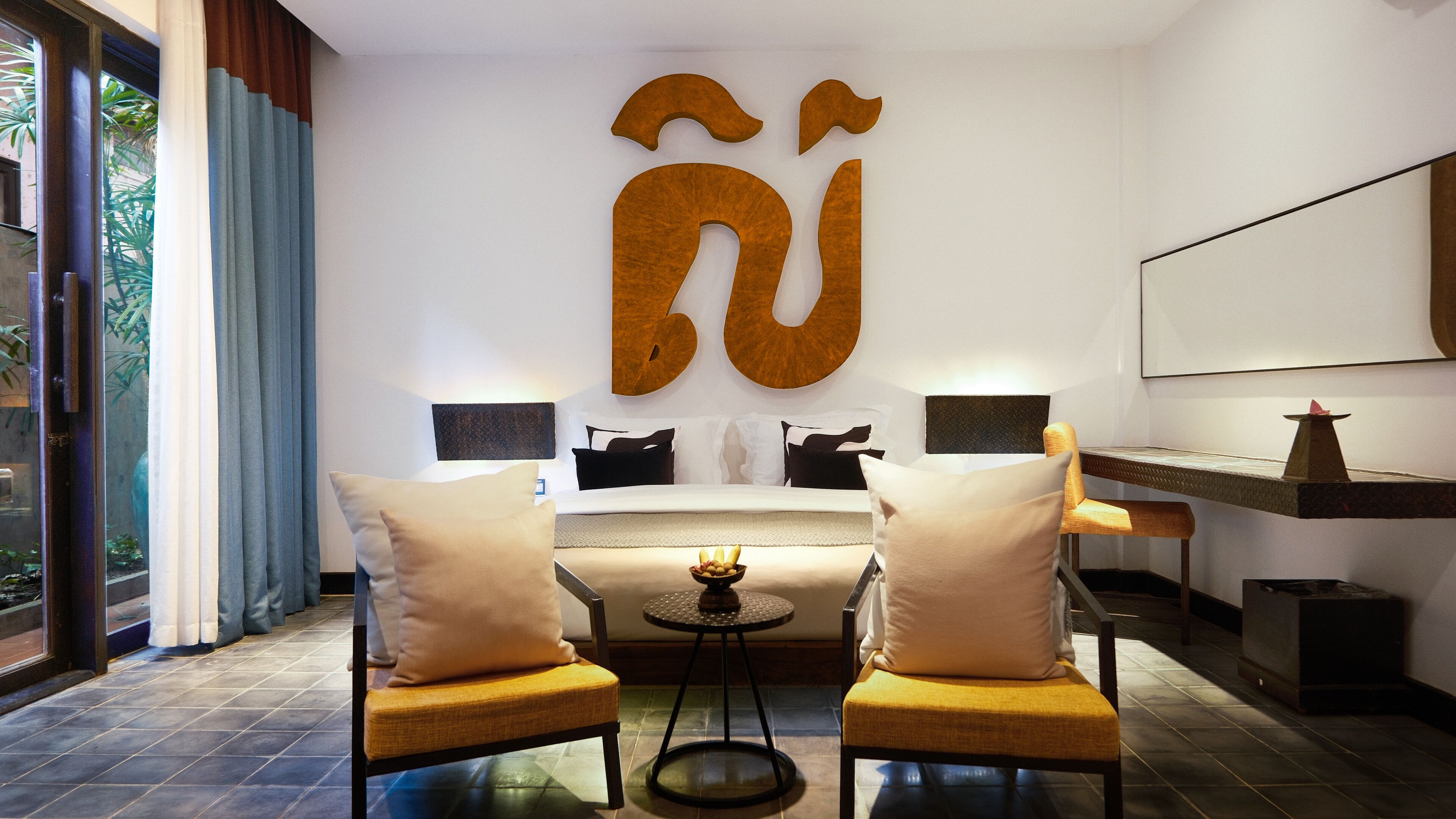 A modern hotel room with a large bed, two armchairs, a small table, and a large wall decoration.