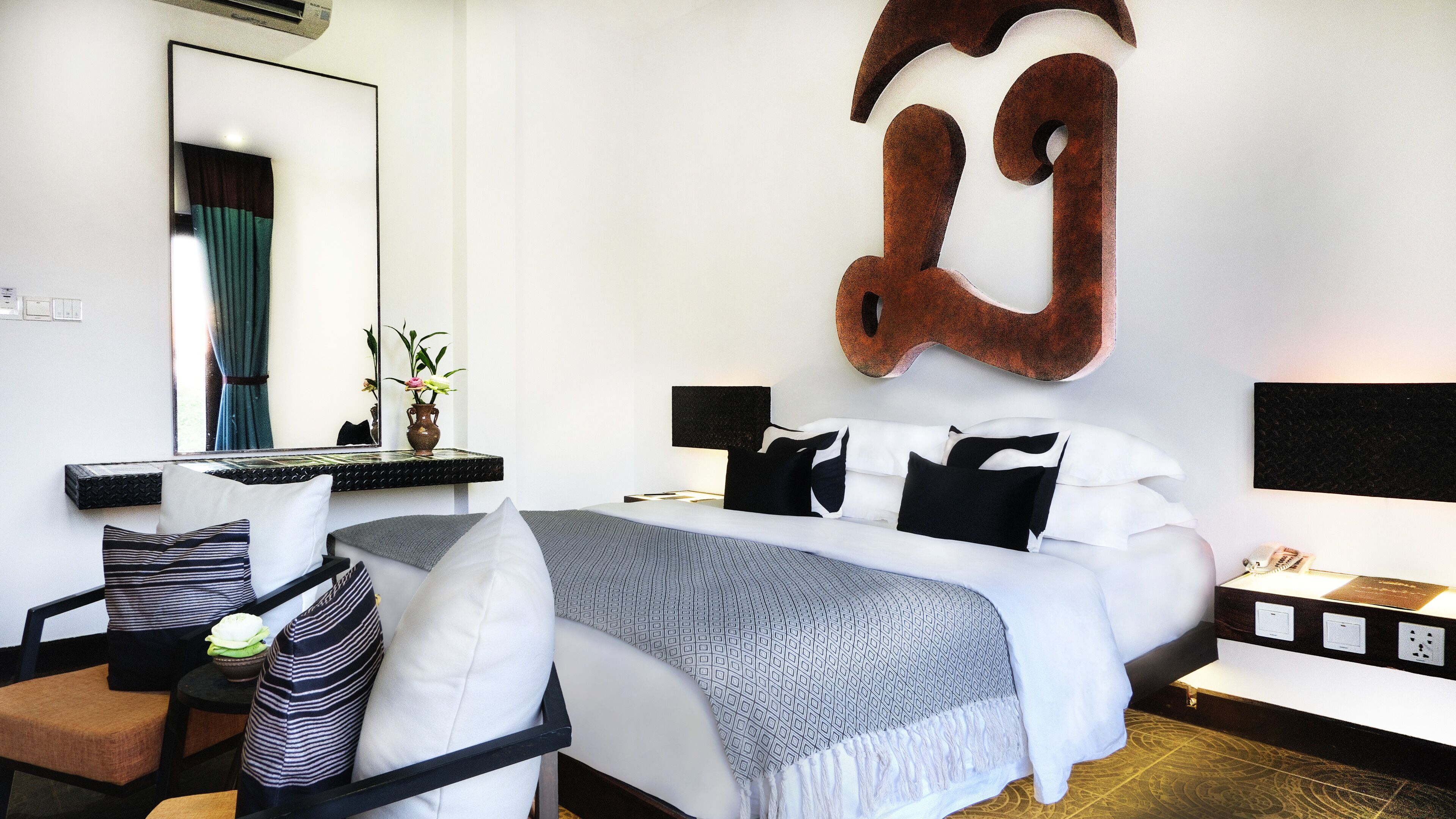 A modern hotel room with a large bed, bedside tables, a desk, and a mirror.