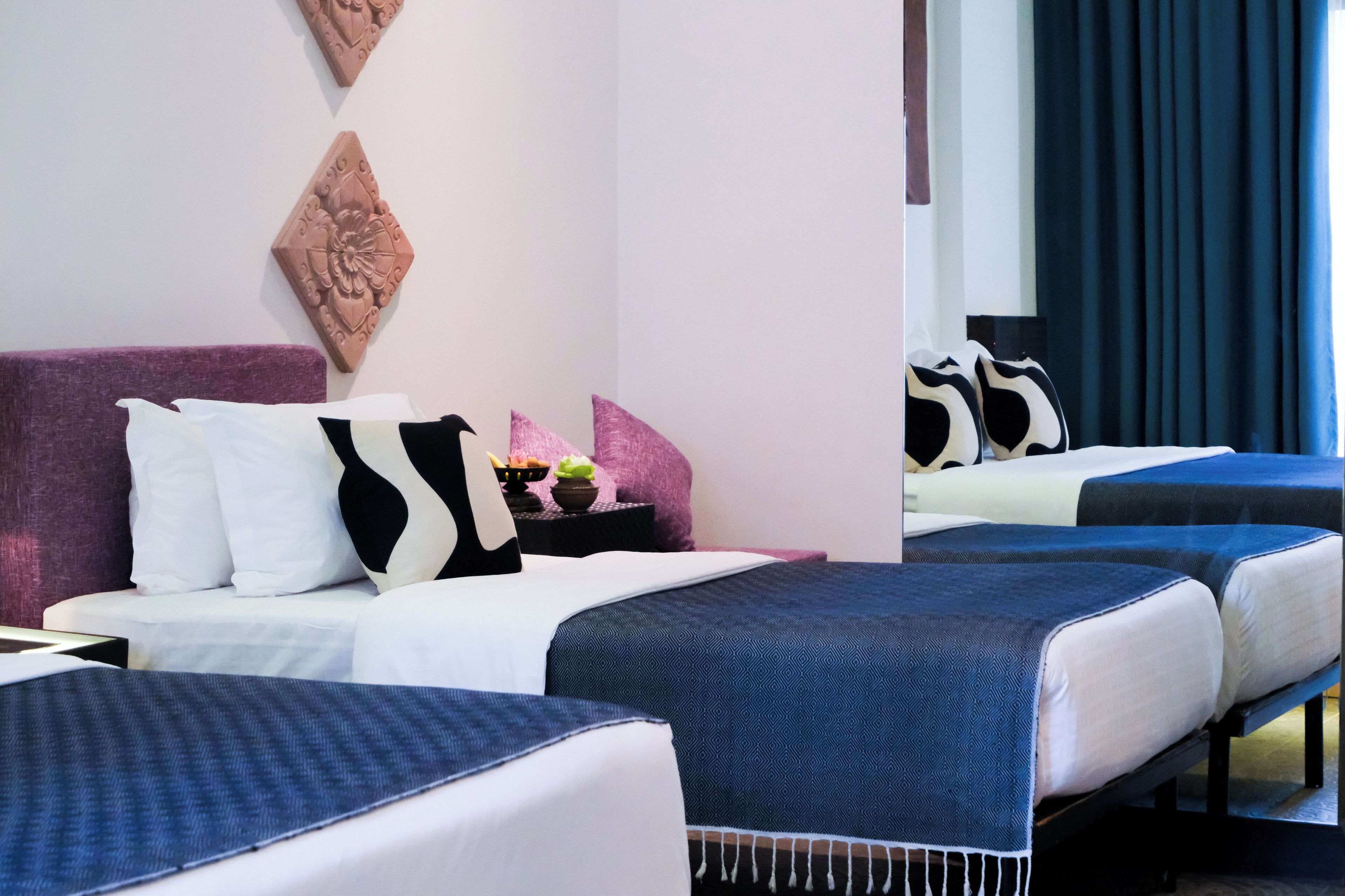 A hotel room with two beds, a purple headboard, decorative wall art, and a nightstand with a lamp.