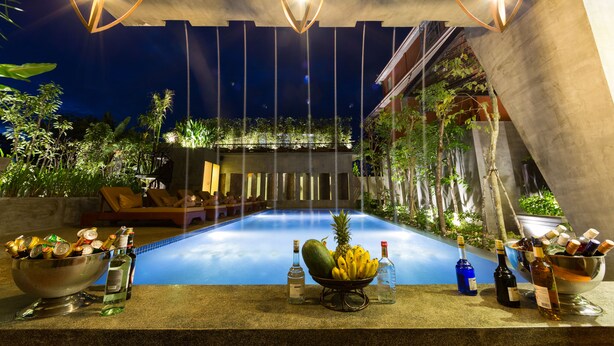 A poolside bar area with a bowl of fruit, bottles of alcohol, and lounge chairs. - Golden Temple Villa (Siem Reap)