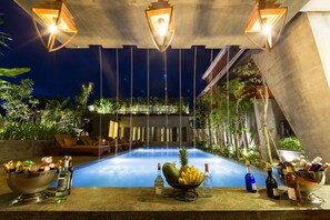 A poolside bar area with a bowl of fruit, bottles of alcohol, and lounge chairs. - Golden Temple Villa (Siem Reap)