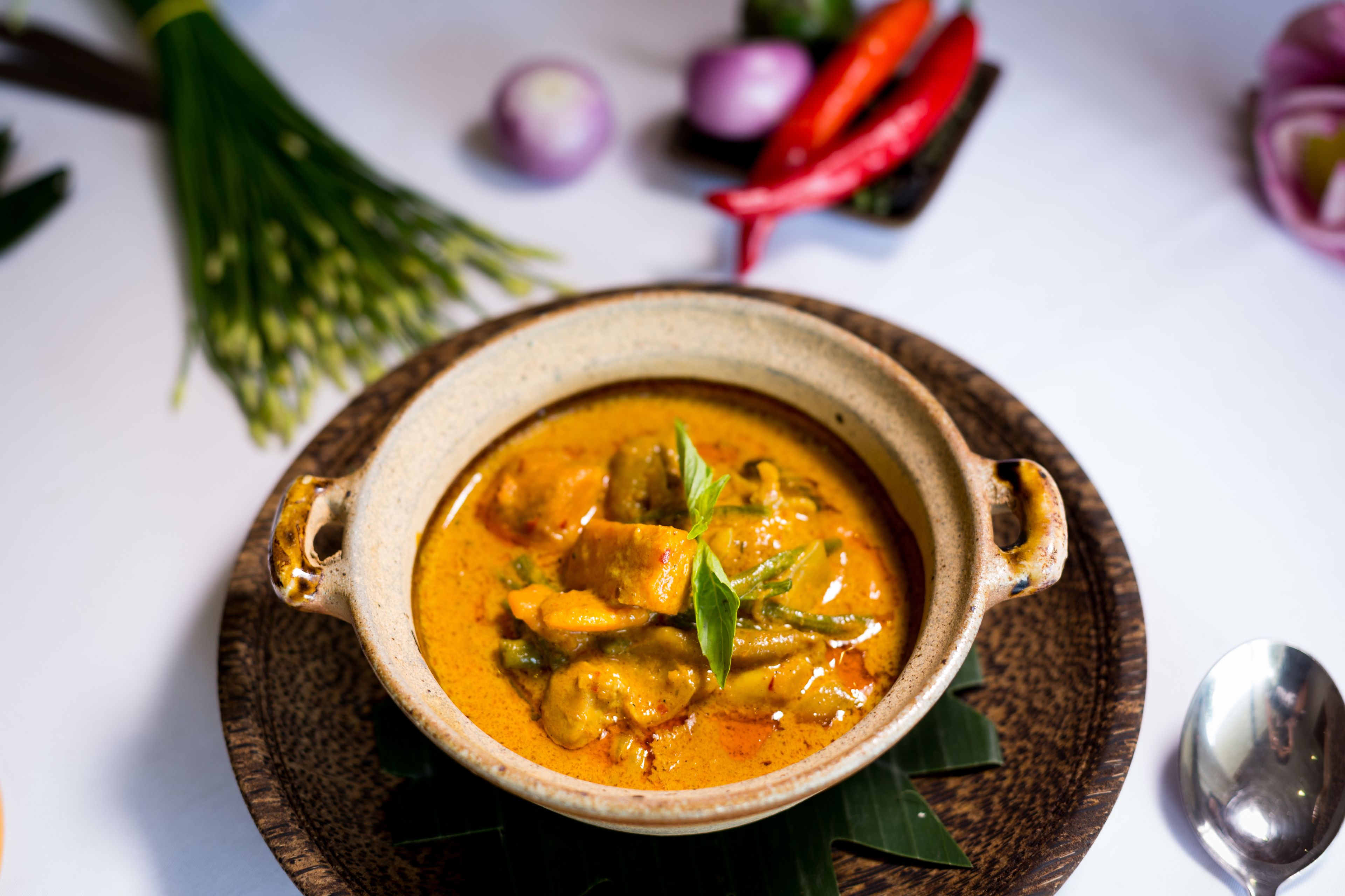 Uma tigela de curry com folhas verdes e pimentas vermelhas ao fundo.