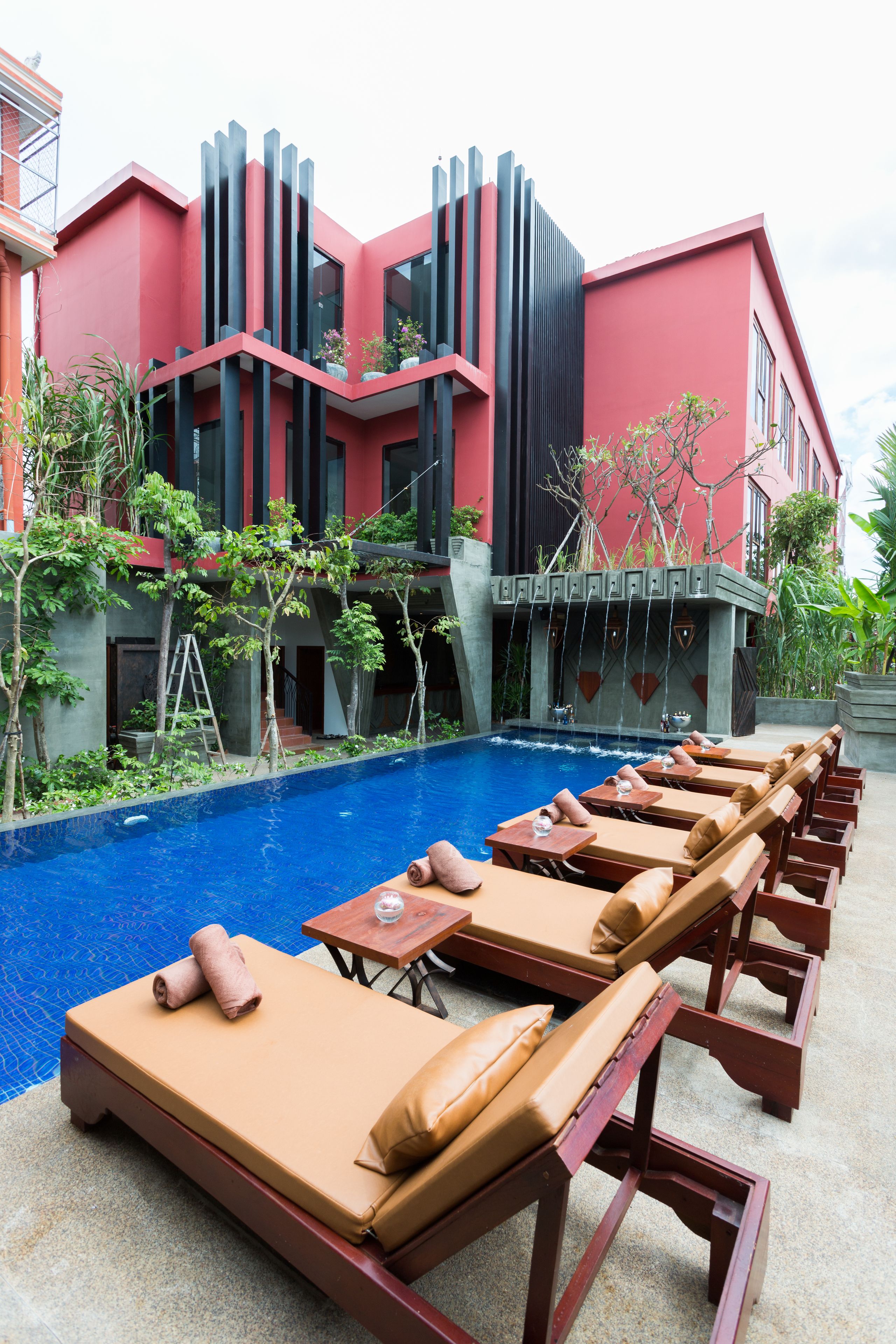 Zona de piscina con sillones de descanso y una piscina, rodeada por un edificio moderno con detalles en rojo y negro.