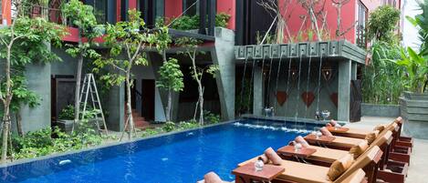Zona de piscina con sillones de descanso y una piscina, rodeada por un edificio moderno con detalles en rojo y negro.